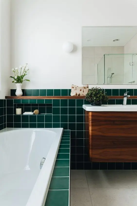 a beautiful modern bathroom clad with green square tiles, with a stained vanity, a shelf and some blooms and plants