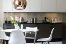 a black and white mid-century modern kitchen with a white dining set, a mosaic tile backsplash and a large copper lamp
