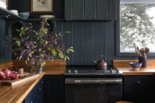 a black farmhouse kitchen done with beadboard, light-colored wooden countertops and stools plus open shelving