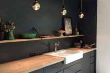 a black kitchen with light-colored wood countertops, pendant lamps and open shelving over the cabinets