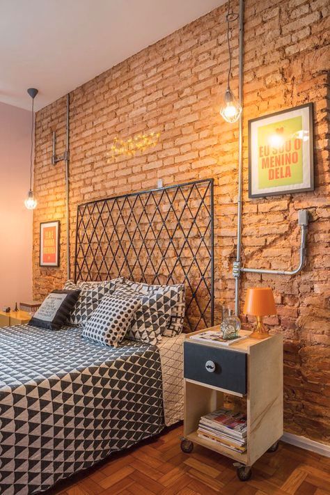 a bold industrial bedroom with red brick walls, exposed pipes, a metal bed, catchy nighstands with casters