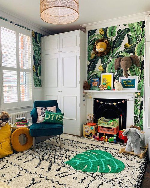 a bold jungle nursery with tropical leaf print walls, layered rugs, colorful animal toys and bright furniture