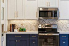 a bold two-tone kitchen with white and navy cabinets, a grey herringbone tile backsplash and white stone countertops