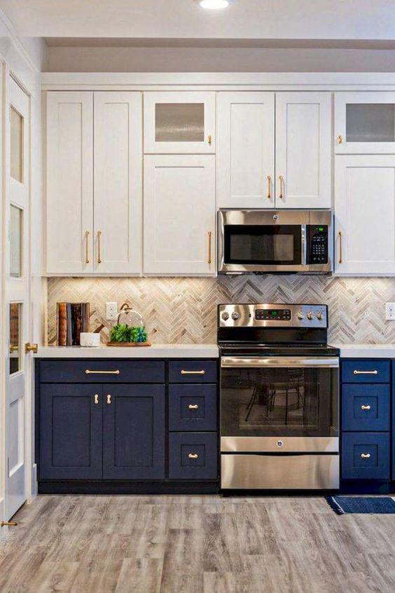 A bold two tone kitchen with white and navy cabinets, a grey herringbone tile backsplash and white stone countertops