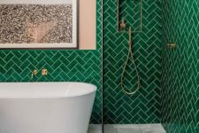 a bright bathroom with emerald tiles in a herringbone pattern, pink walls, gold touches and a white tub