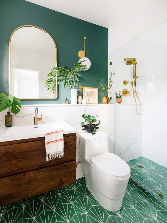 a bright ggreen bathroom with a green wall, a green mosaic tile floor, a wooden vanity and touches of gold and brass