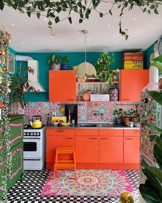 a bright orange kitchen with colorful mismatching tiles, blue walls, a green sideboard, potted plants and a colorful rug