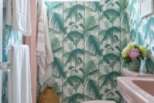 a bright tropical bathroom with tropical wallpaper, a pink sink and toilet, neutral linens