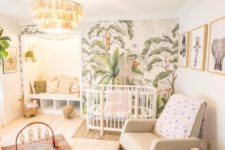 a bright tropical nursery with a tropical printed wall, a tassel chandelier, boho rugs, a leather ottoman and printed pillows