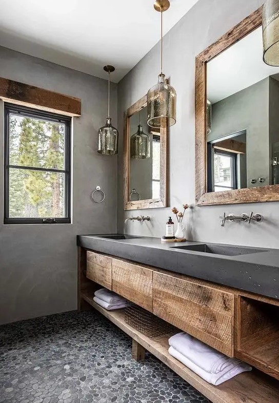 a catchy bathroom with concrete walls and a vanity, wooden storage units, pendant lamps and mirrors in rough wooden frames