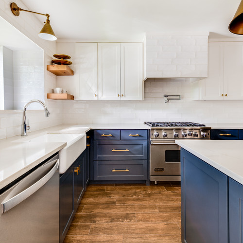 a catchy kitchen with white and navy shaker style cabinets, a white tile backsplash and countertops and gold handles