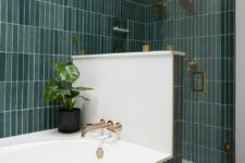 a catchy modern bathroom clad with green skinny tiles, a shower space, gold and brass fixtures and potted plants