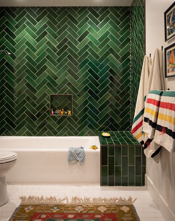 a catchy modern tub with green tiles clad in a herringbone pattern, a white tub and white tile floor