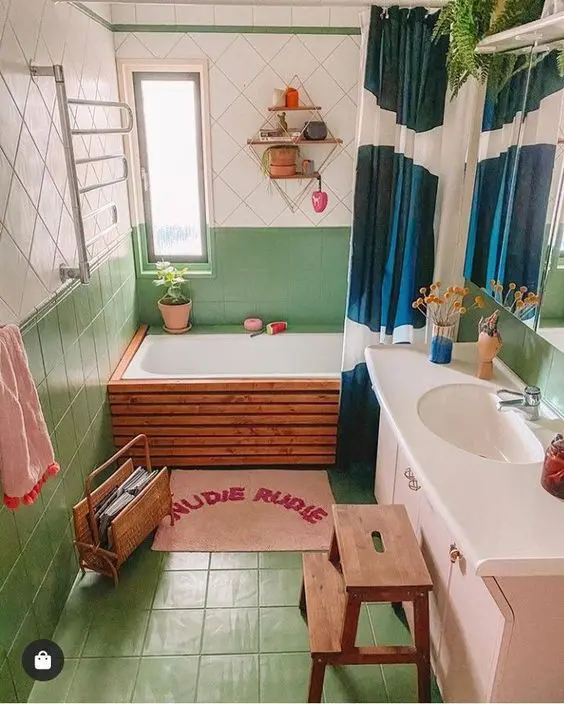 a chic and bold bathroom with green and white tiles, a pink vanity, a ladder, a magazine stand and a bold printed curtain