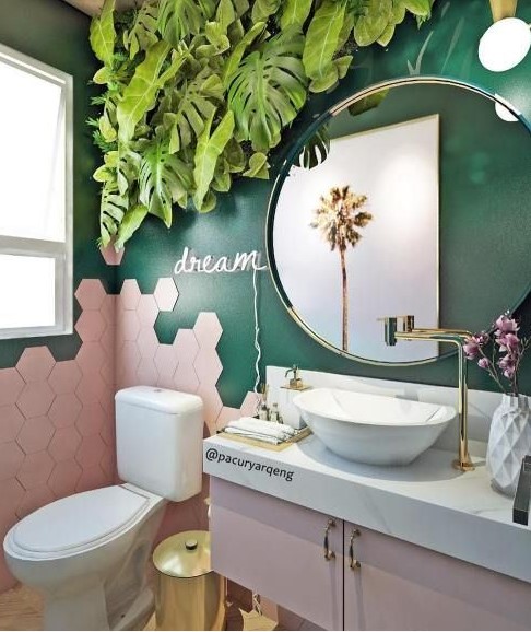 a chic and fun tropical bathroom with emerald walls, pink hex tiles and a pink vanity, a tropical leaf decoration and gold touches