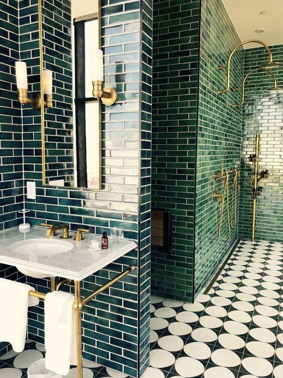 a chic art deco bathroom with dark green tiles, gold and brass touches, a stone vanity and black and white mosaic tiles