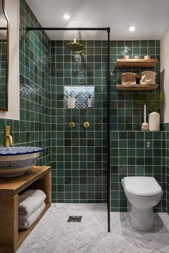 a chic bathroom with dark green tiles, a wall mounted vanity, a Moroccan sink, stained shelves and gold fixtures