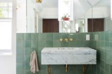 a chic bathroom with pale green tiles, mosaic tiles on the floor, a marble vanity and sink in one plus brass touches