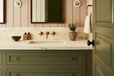 a chic bathroom with pink shiplap walls, an olive green vanity and a matching door, sconces and baskets