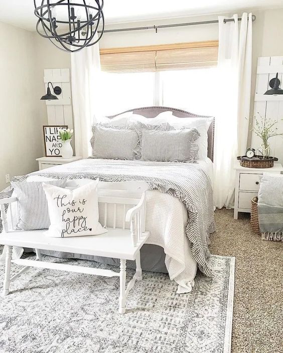 a chic farmhouse bedroom done in white, with vintage furniture, a sphere chandelier, baskets for storage and artworks