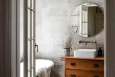 a chic grey bathroom clad with grey concrete tiles, an oval tub, a stained vanity, a round mirror and a pendant lamp