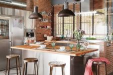 a chic industrial kitchen with red brick walls, metal cabinets and appliances, exposed pipes and metal stools