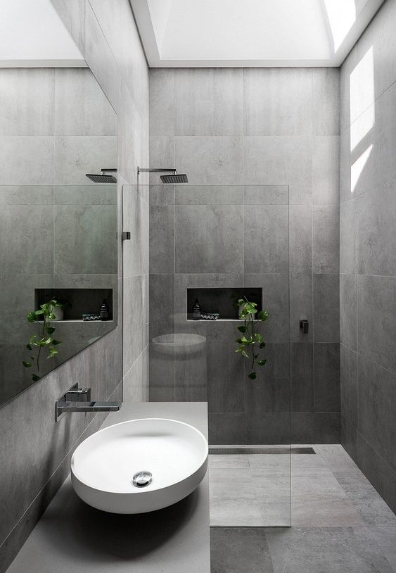 a chic minimalist grey bathroom with large scale tiles, a grey vanity with a round sink and some potted greenery