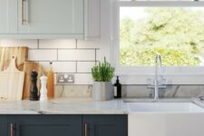a chic two tone kitchen with light green and graphite grey shaker cabinets, a white subway tile backsplash and white marble countertops