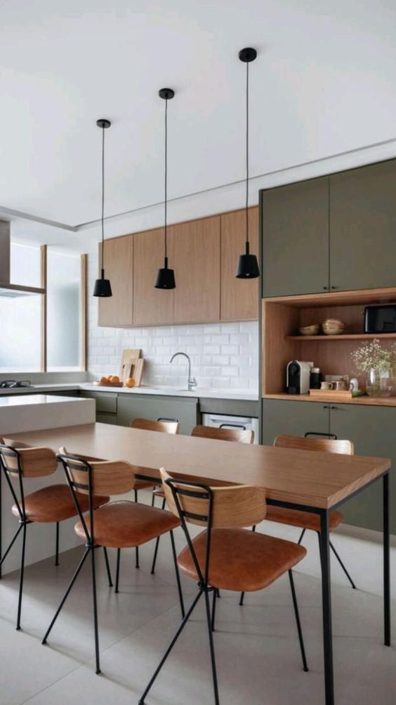 a chic two-tone kitchen with olive green and stained cabinets, a kitchen island with a dining table and black lamps