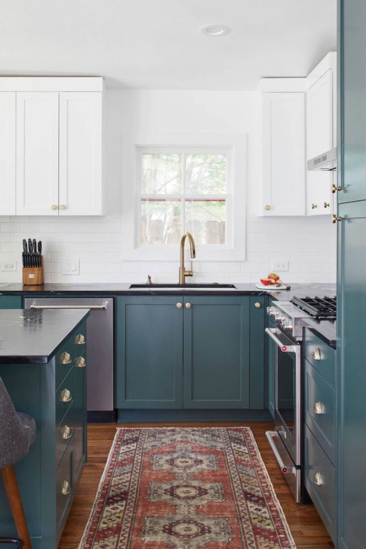 A chic two tone kitchen with teal and white shaker style cabinets, a white tile backsplash and a bold rug