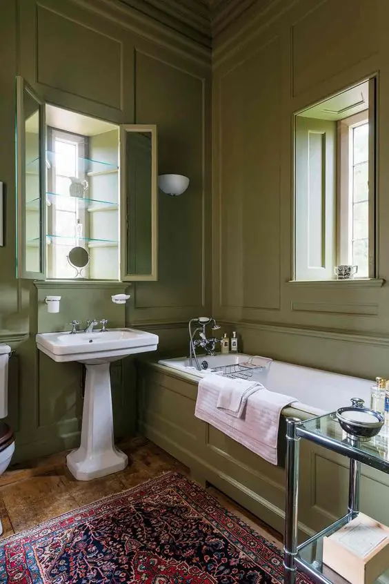 a chic vintage bathroom with green grass paneled walls, a free-standing sink, a tub clad with panels and a bold rug