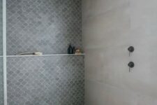 a concrete bathroom with an accent fish scale tile wall and dark brass fixtures is a pretty and cool space