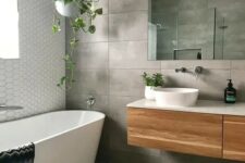 a concrete tile bathroom with an oval tub, a floating vanity, a mirror and some potted greenery is cool