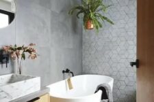 a contemporary bathroom clad with concrete tiles, with a geometric accent wall, a floating vanity with a marble sink, a tub and potted plants