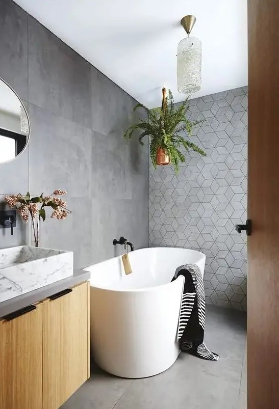 a contemporary bathroom clad with concrete tiles, with a geometric accent wall, a floating vanity with a marble sink, a tub and potted plants