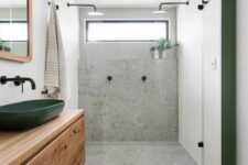 a contemporary bathroom done with grey terrazzo, a window, a floating timber vanity, a dark green sink and a matching door frame