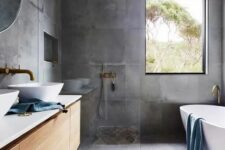 a contemporary bathroom with a concrete floor and walls, a floating vanity and brass fixtures plus an oval tub
