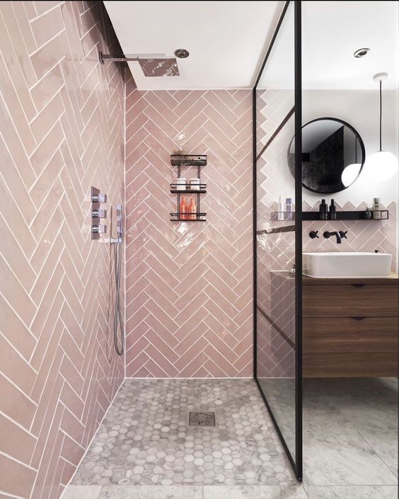 a contemporary bathroom with pink tiles clad in a herringbone pattern, with black touches and a wooden floating vanity