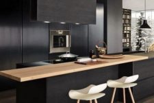 a contemporary black kitchen with sleek cabinets, built-in appliances, a light-colored wood countertop and a black hood