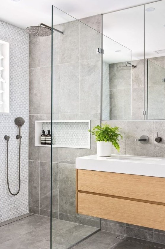 a contemporary grey bathroom clad with large scale tiles and penny ones, with a floating wooden vanity and a large window