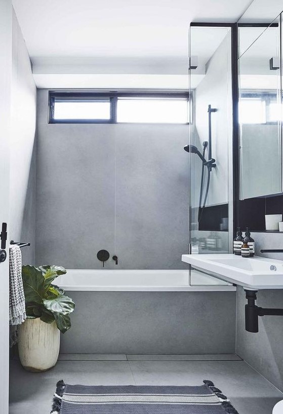 a contemporary grey bathroom clad with large scale tiles, with a small window and black fixtures to make it look bolder