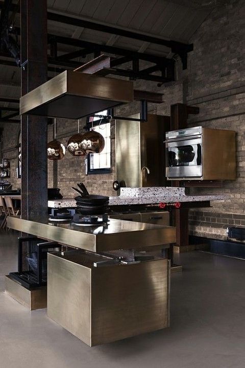 a contemporary industrial kitchen with brick walls, shiny metal cabinets and a hood, bright terrazzo ocuntertops and copper lamps