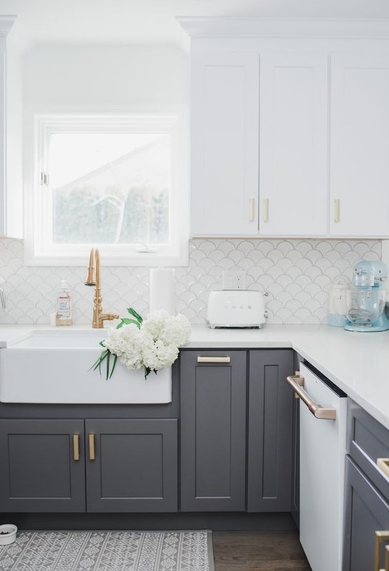a contemporary kitchen with white upper cabinets and lower grey ones, gold and brass handles plus a white fish scale backsplash
