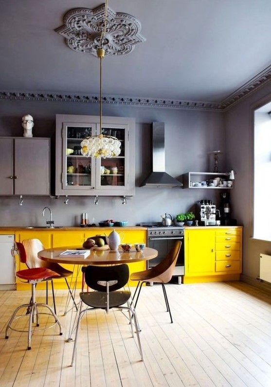 a contrasting and moody kitchen with grey walls and a ceiling, upper cabinets and lower yellow ones, mismatching chairs