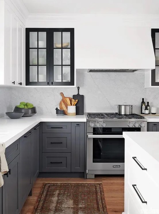 a contrasting kitchen with white upper cabients and charcoal grey ones, black glass frame cabinets and a white backsplash and countertops