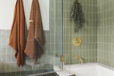 a cool bathroom with green tiles cladding the walls and tub, gold and brass fixtures is a cool and lovely space