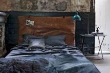 a cool industrial bedroom with shabby chic walls, a leather upholstered bed, a metal lamp and table and dark bedding
