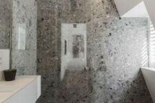 a cool minimalist grey bathroom with grey terrazzo in the shower, a white vanity and windows for natural light