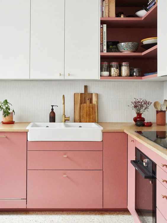 a cool two-tone kitchen with pink and white sleek cabinets, a white skinny tile backsplash and butcherblock countertops