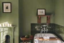 a cool vintage bathroom with moody green walls and green tiles, a bathtub, a fireplace and some artwork is cool